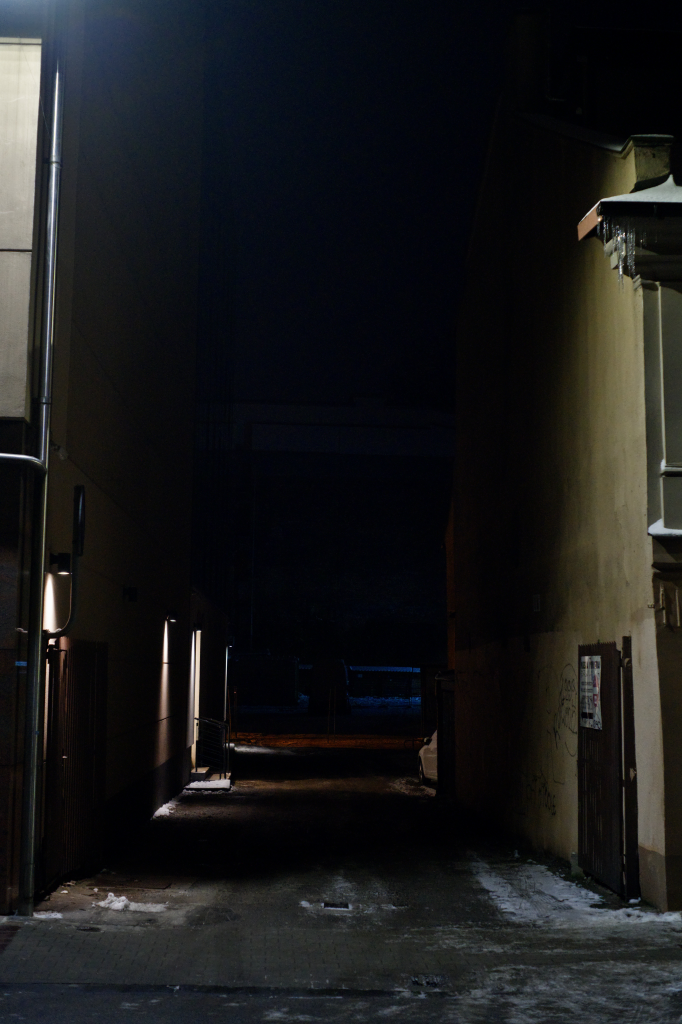 A dark alleyway with irregular splotchy shadows.
